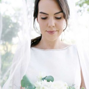 Woman in white dress holding a bouquet of white flowers and greenery with a sheer veil.