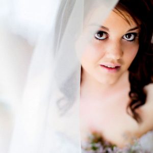 Close-up of a woman with dark hair and makeup partially obscured by translucent white fabric.
