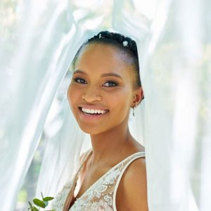 Bride smiling wearing a white lace wedding dress, veil, hair accessories, and earrings.