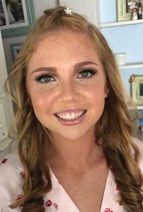 Young woman with freckles, green eyes, curly light brown hair, wearing a pink cherry-patterned top.