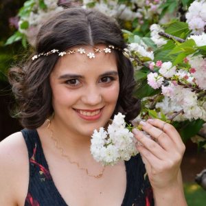 Young woman with floral headband holding white blossoms near flowering shrub outdoors.