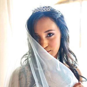 Woman with long dark hair wearing a tiara and sheer white veil partially covering her face.