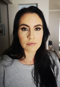 Close-up of a woman with long dark hair and brown eyes wearing a light gray sweater indoors.