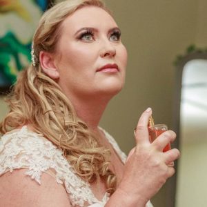 Woman with curled blonde hair in white lace garment spraying perfume and looking upward